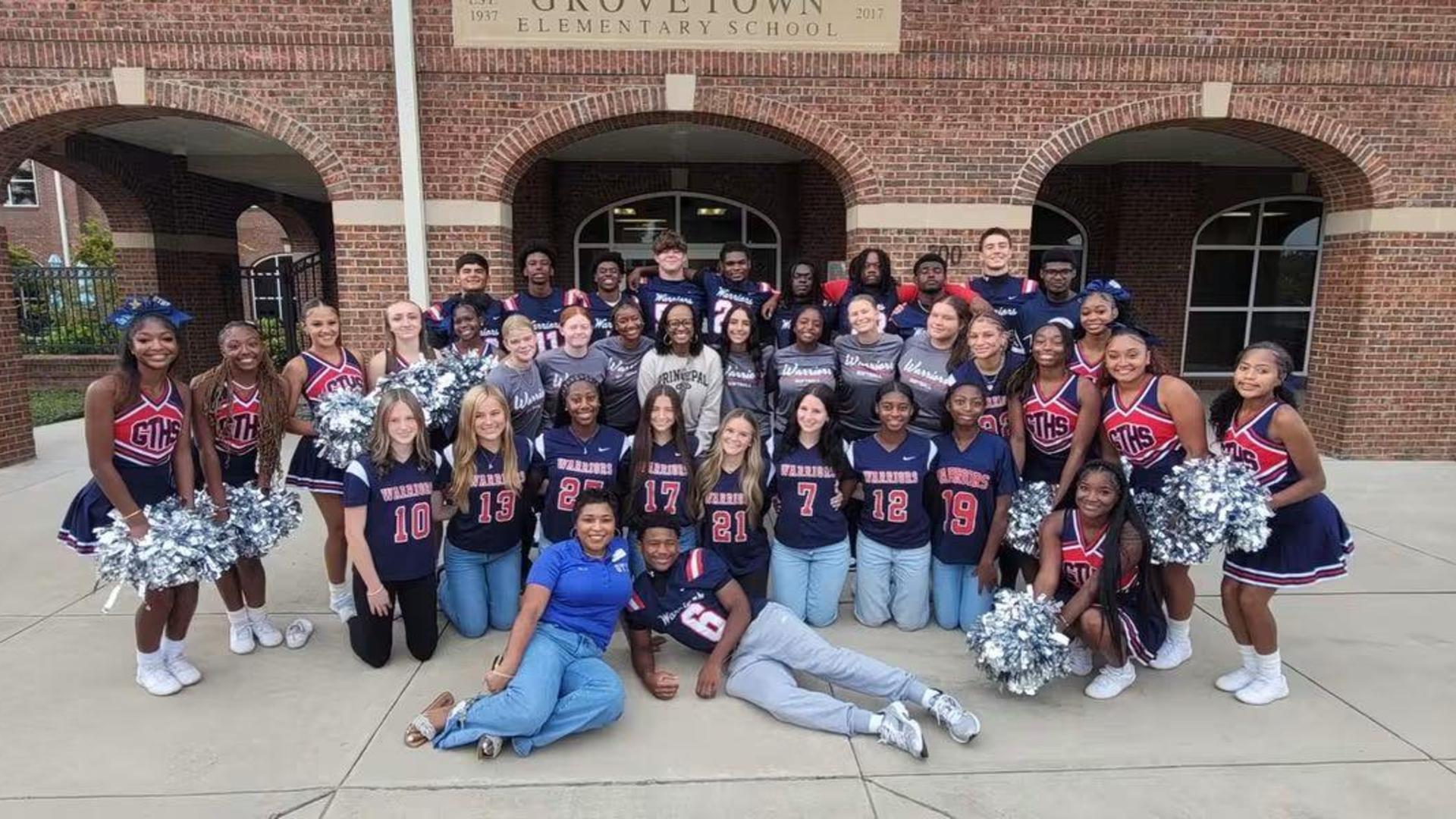 Group photo of students and cheerleaders in school uniforms outside an elementary school.