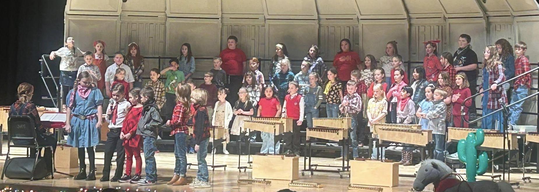 A large group of children performing on stage with musical notes in the background.