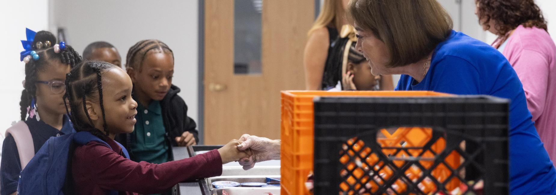 A cafeteria worker shakes the hand of an elementary student