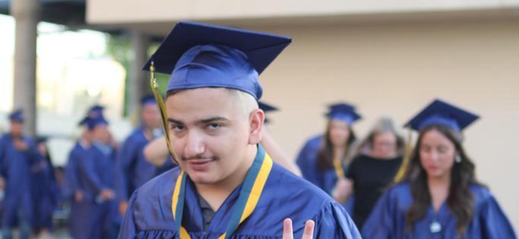 Graduate in cap and gown making a peace sign while walking with peers.