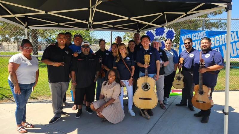 group of more than 10 persons some holding musical instruments under a tent