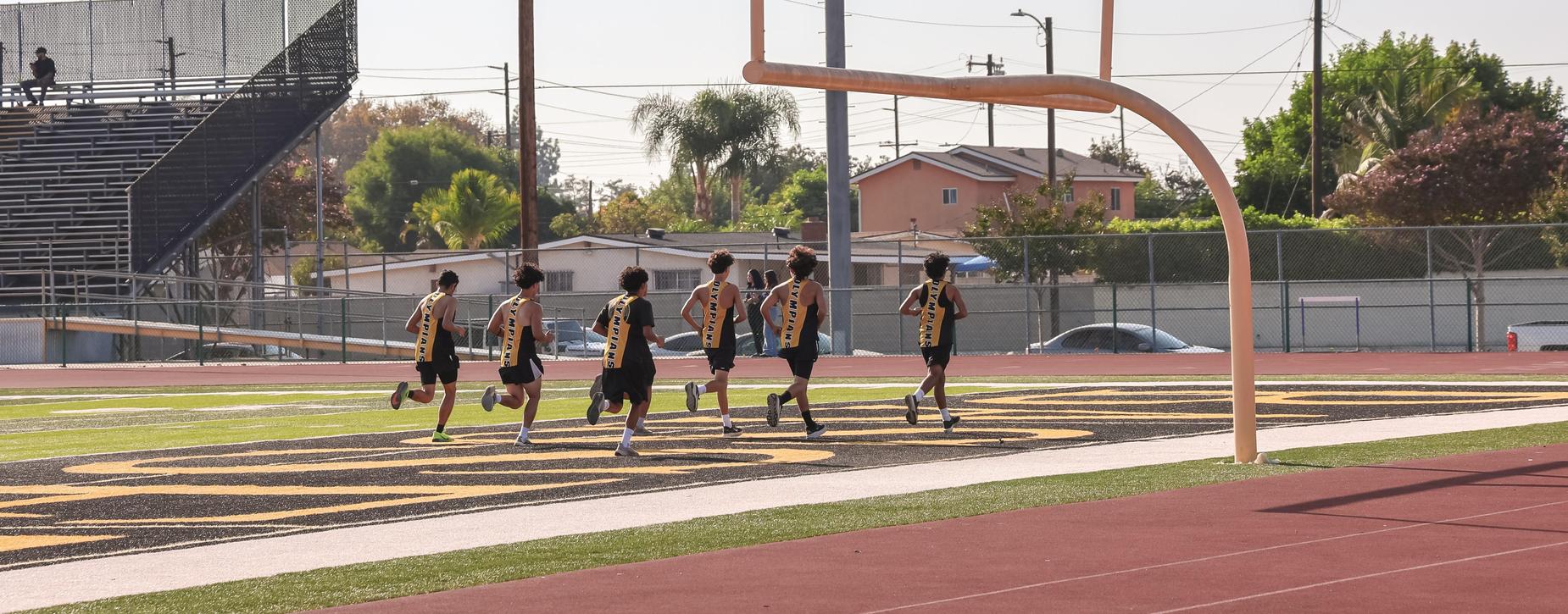 A group of runners training on a track near a football goalpost.