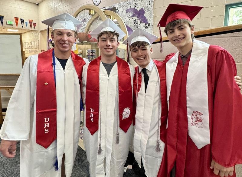 Four graduates stand together in a hallway