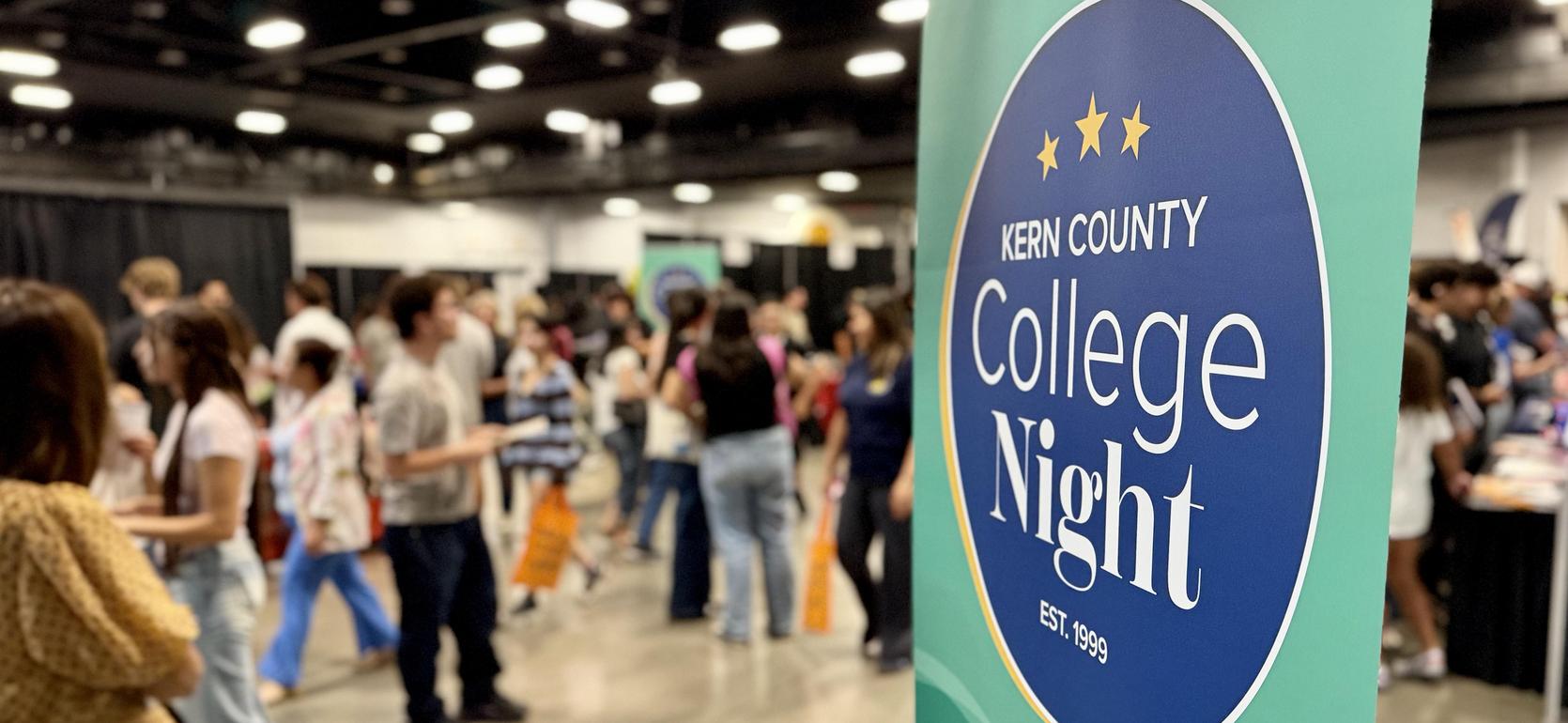 Kern County College Night sign with attendees in the background.