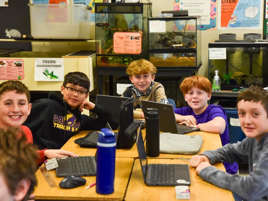 Students sitting at a classroom table with Chromebooks open and various aquariums in the background.