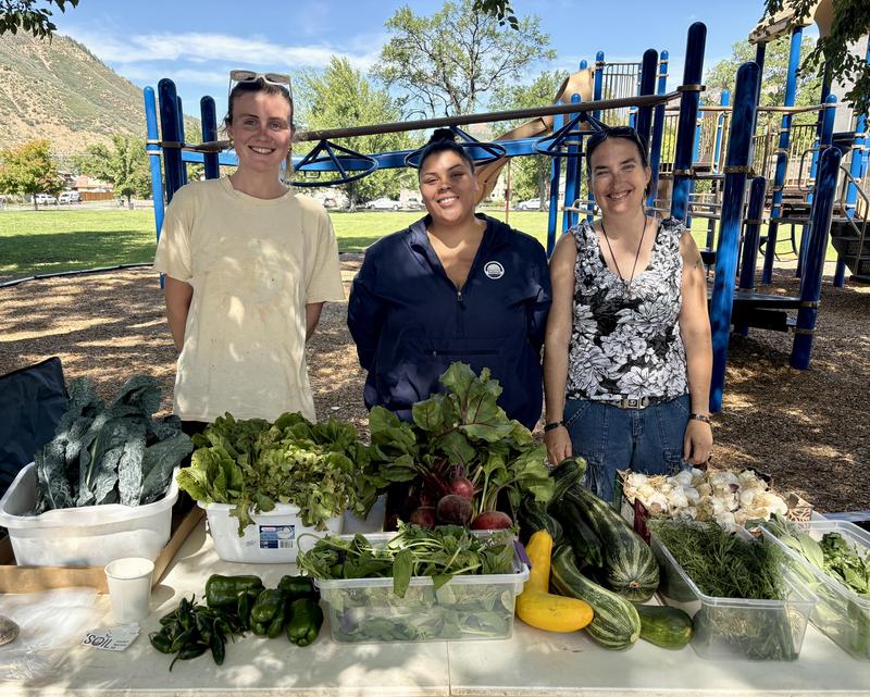 a man and two women stand in front of a table fllled with fresh produce