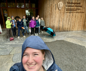 Group of children and adults smiling outside a wooden building.