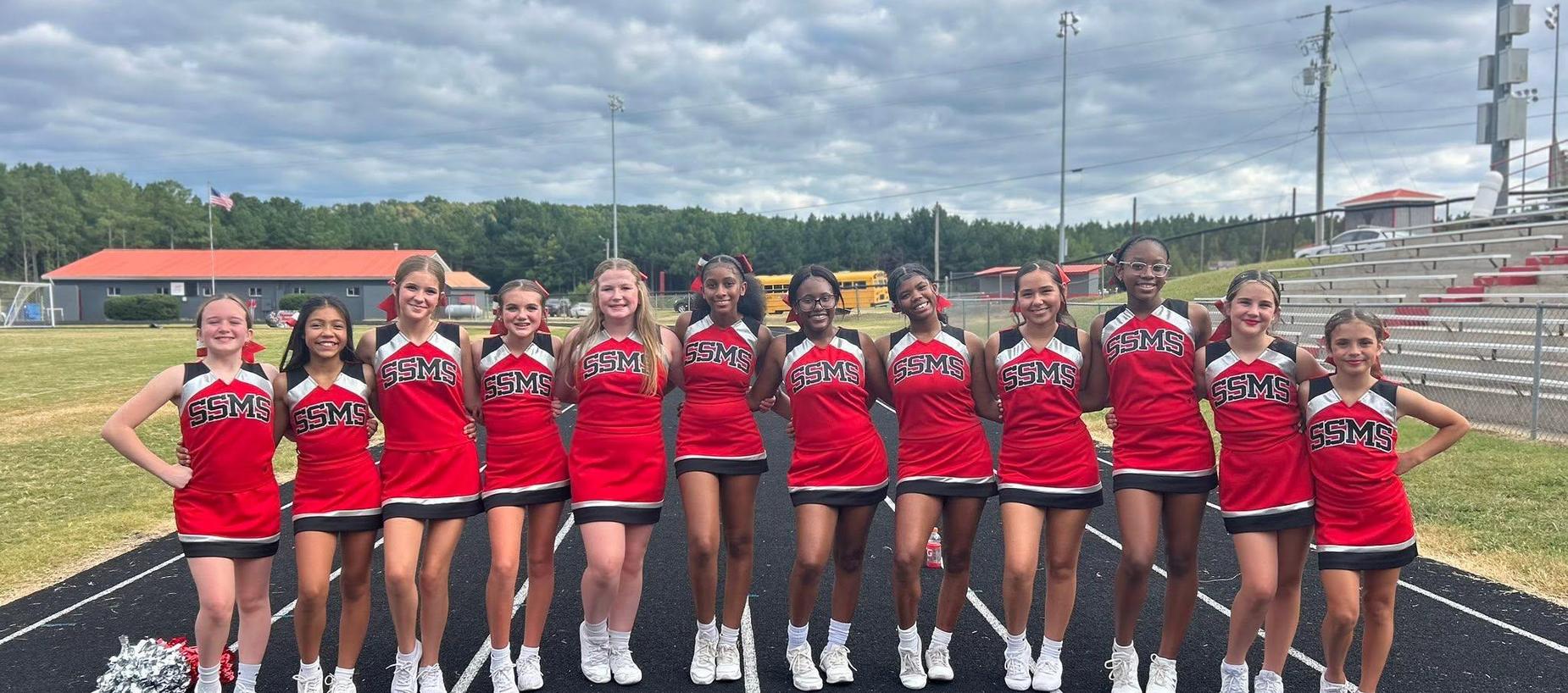 A cheerleading squad in red and black uniforms poses together on a track.