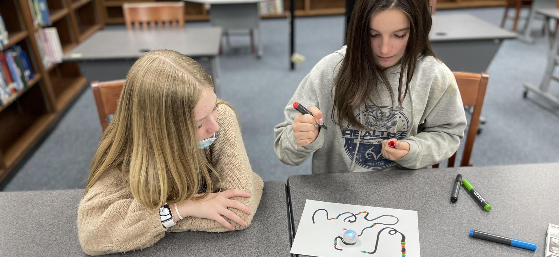 Two students write code for a robot.