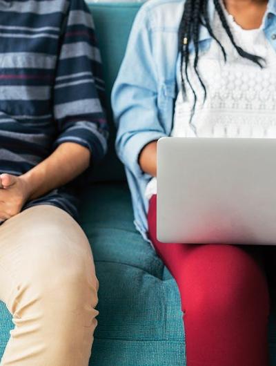 Two people sitting on a couch, one using a laptop while the other is resting.