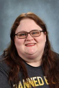 Smiling woman with glasses and long brown hair in a dark shirt.