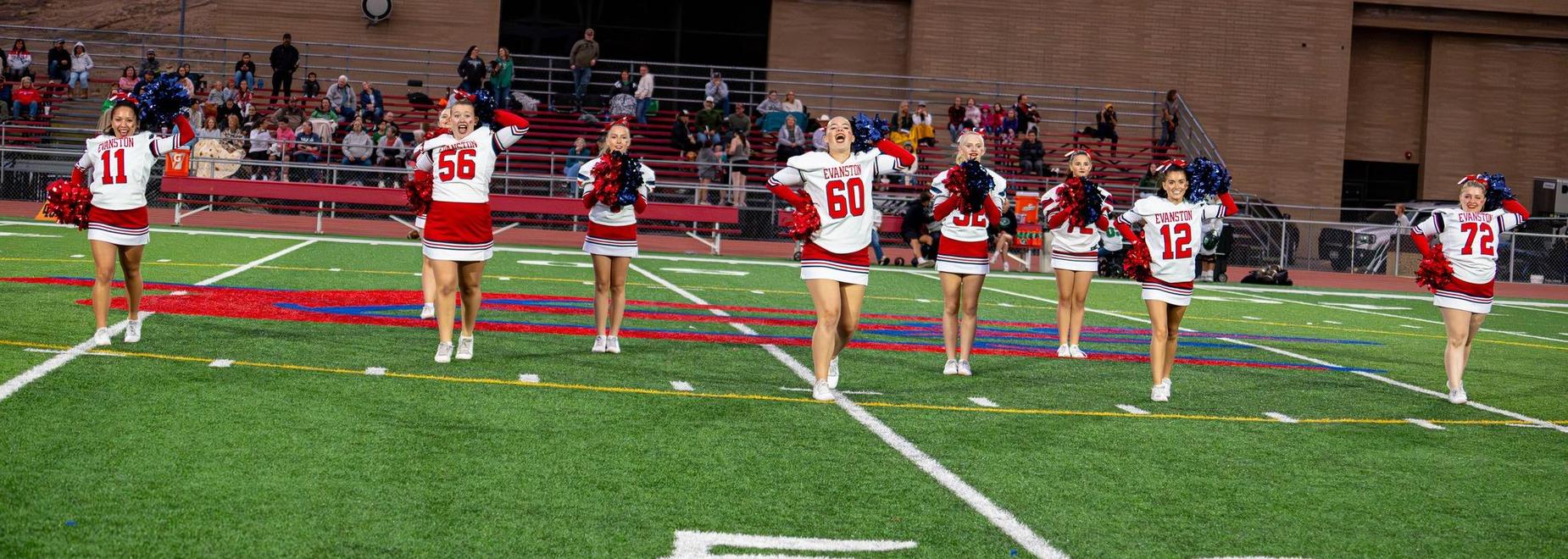 Cheerleaders celebrating in unison on the football field in uniforms.