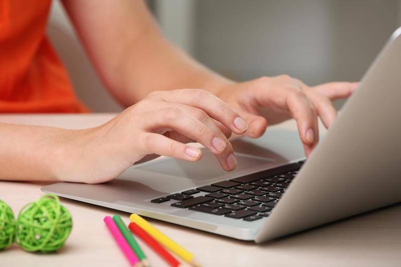 A person is seated, using a laptop. There are pencils and other school supplies nearby.