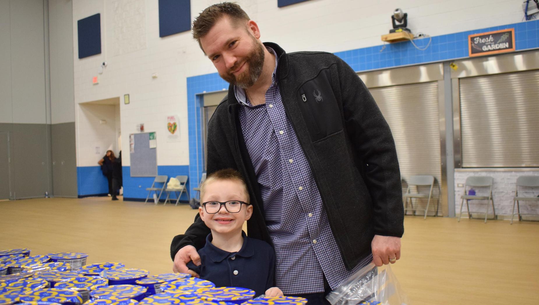 A man and a boy smiling together near a table with blue containers.
