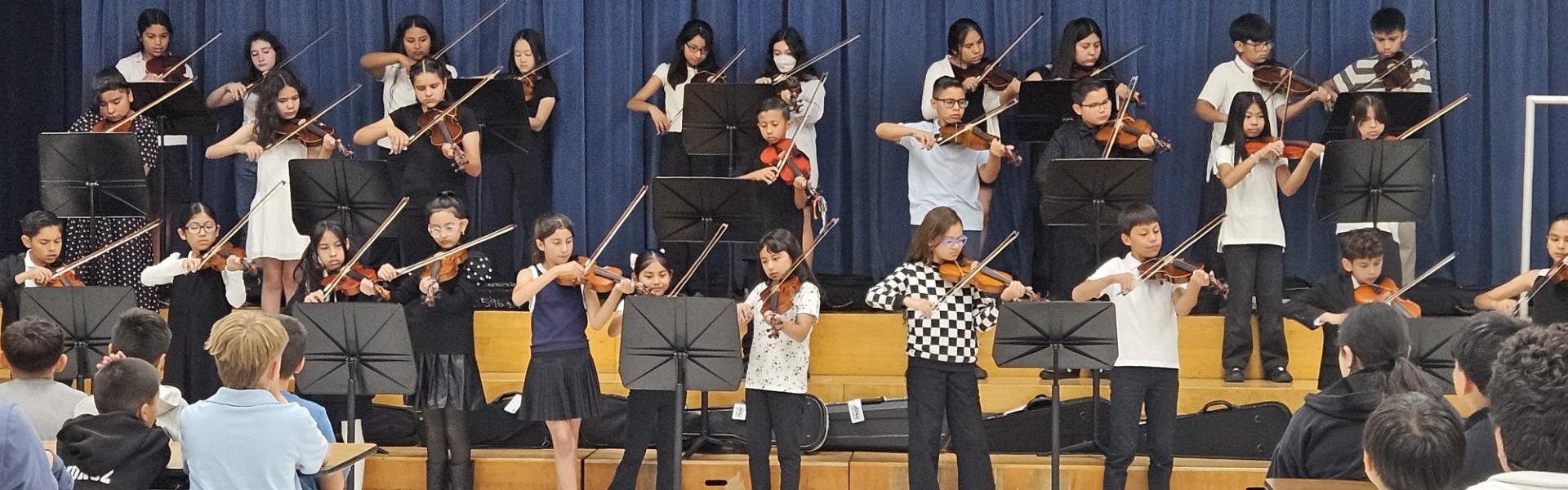 A group of children playing violins during a performance on stage.