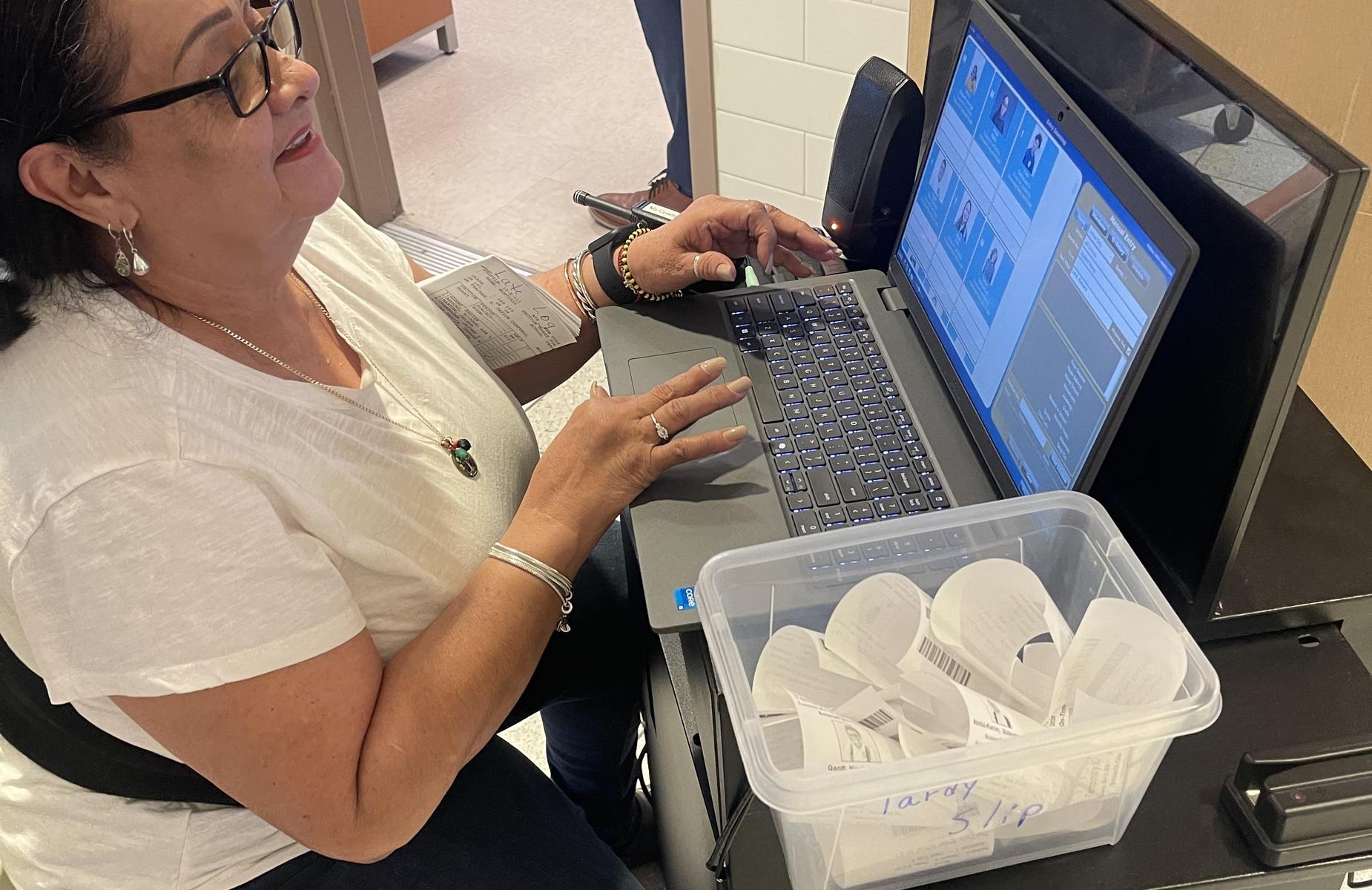 A woman types on a laptop while seated, with receipts in a bin nearby.