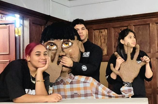 Three students posing with a life size puppet that they created.