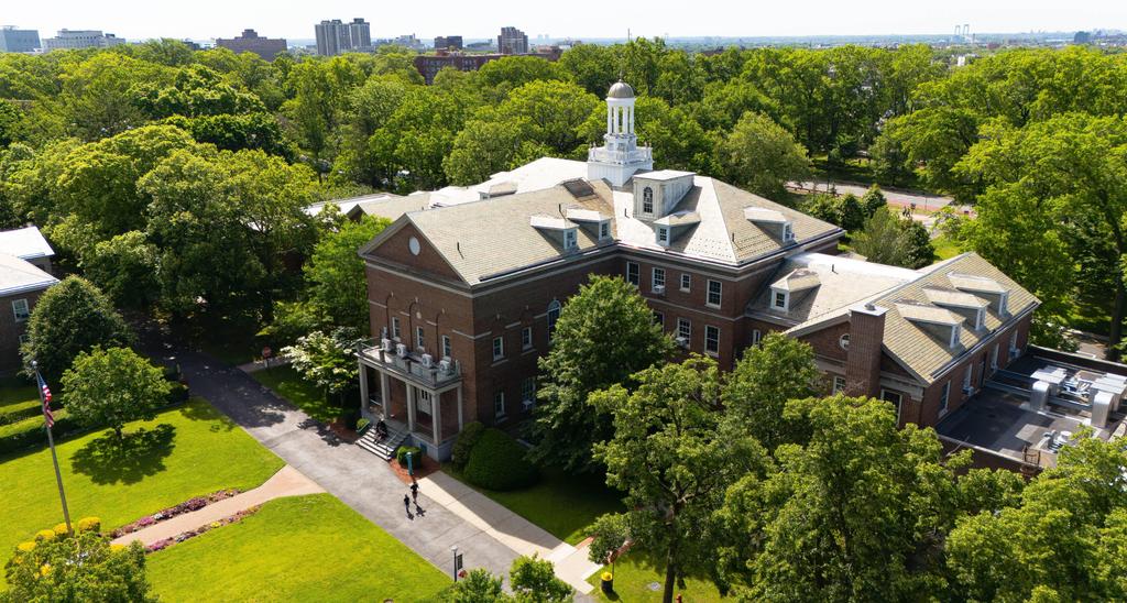 Aerial view of a brick building surrounded by trees and greenery.