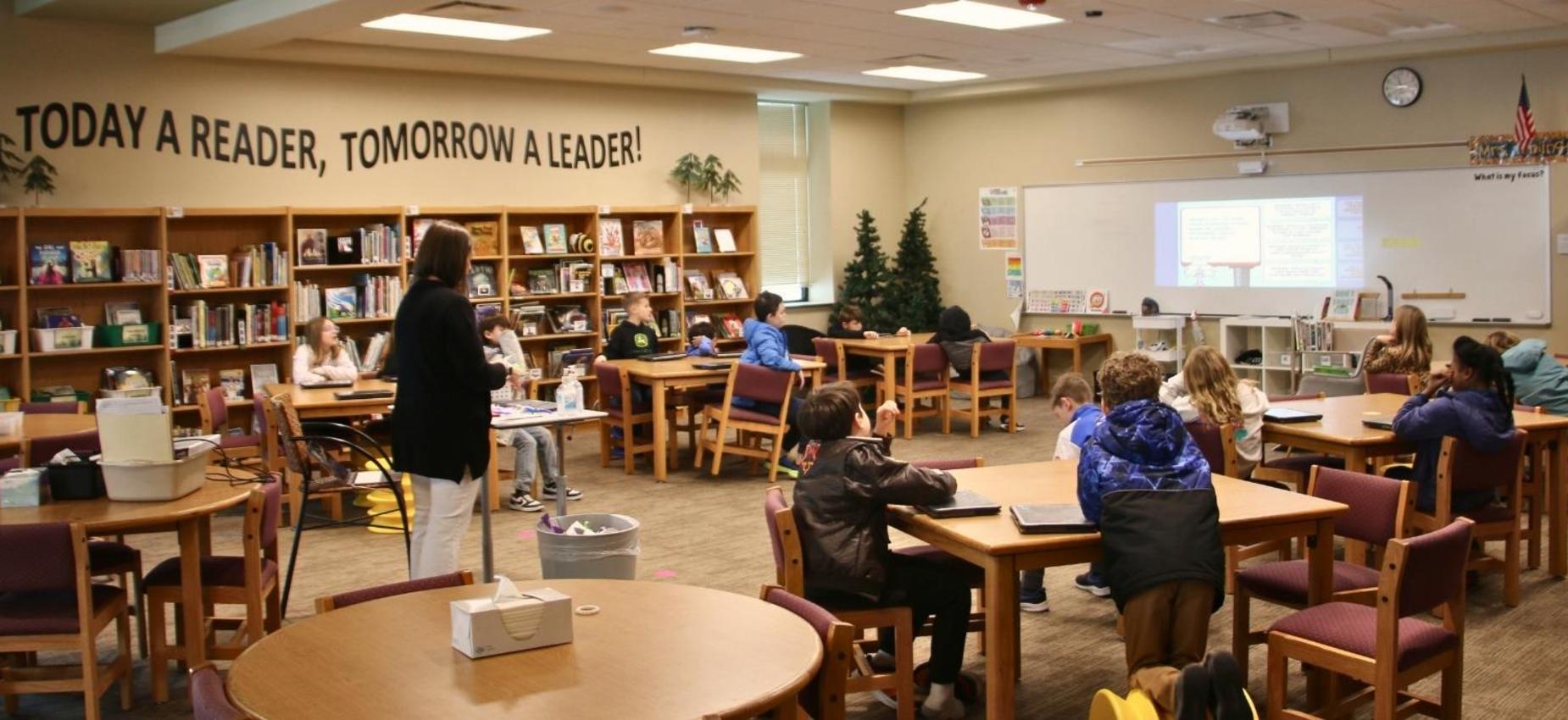 Classroom with students engaged in learning, shelves of books in the background.