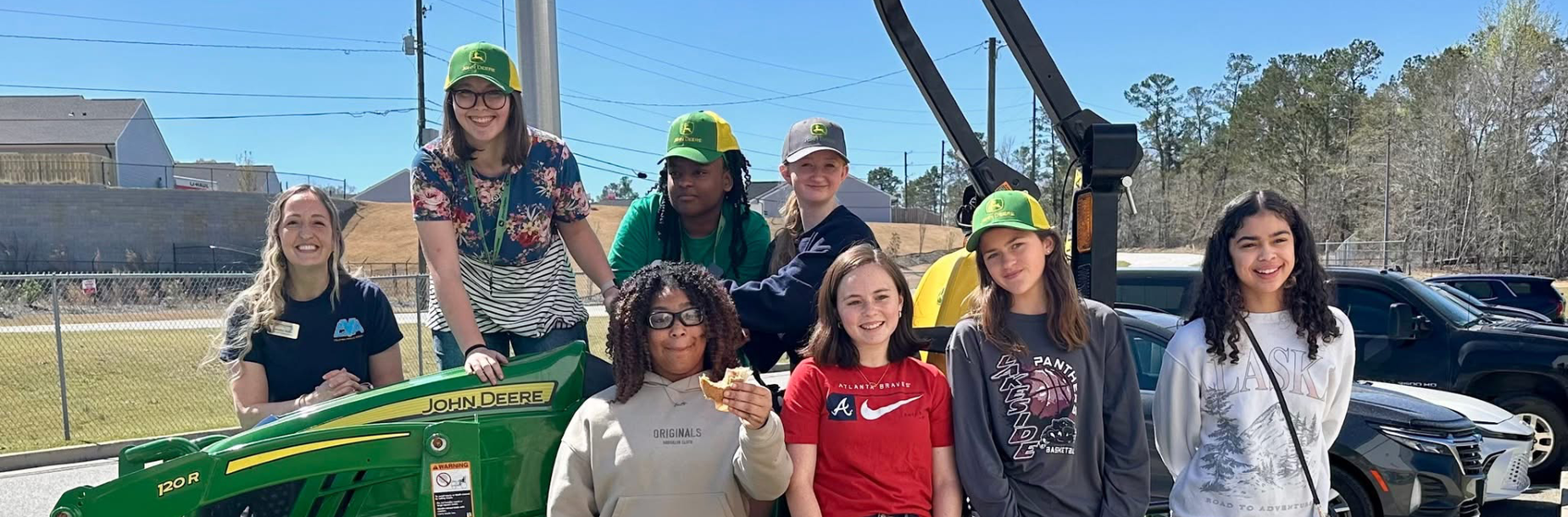 Group of young people posing on a tractor with smiles and casual clothing.