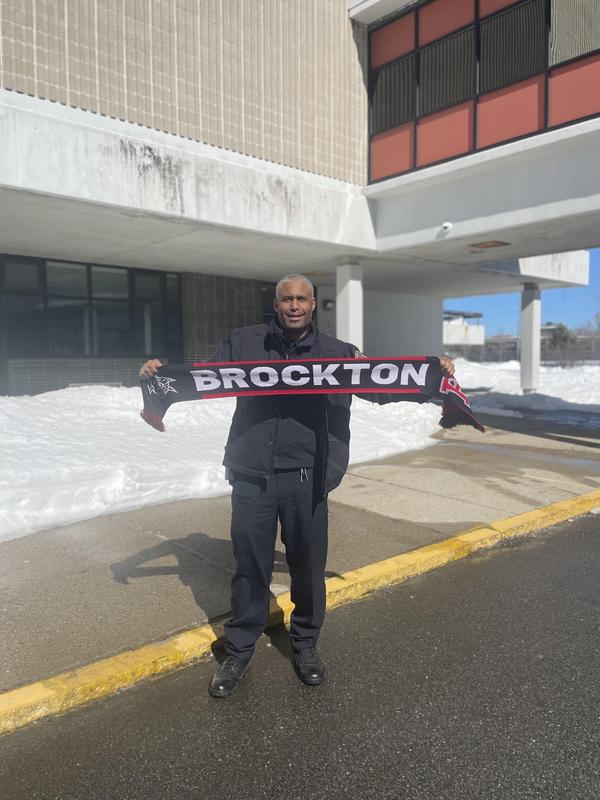 Police officer stretching out a black scarf that says "BROCKTON" with a Boxer on it