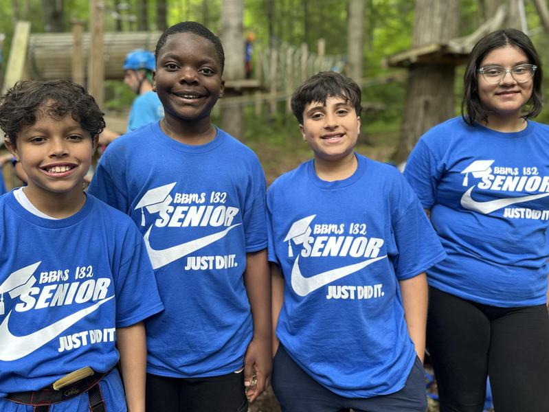 Four children in blue shirts with 'SENIOR' printed on them, smiling outdoors.