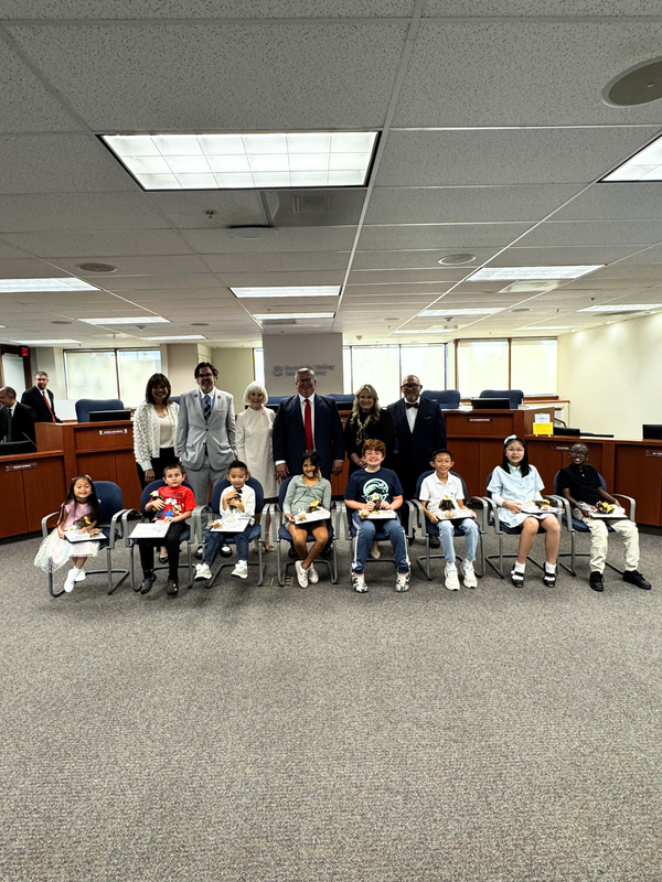Group of children and adults posing in a courtroom setting, smiling and holding certificates.
