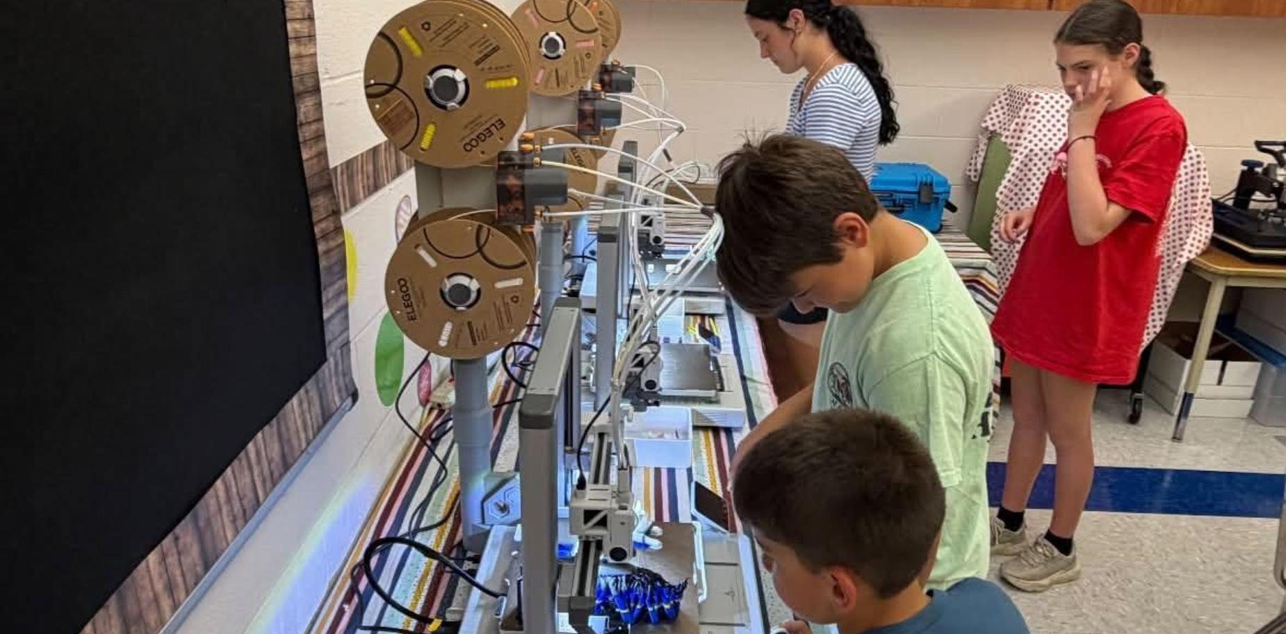 Children and teens working on 3D printers in a classroom setting.