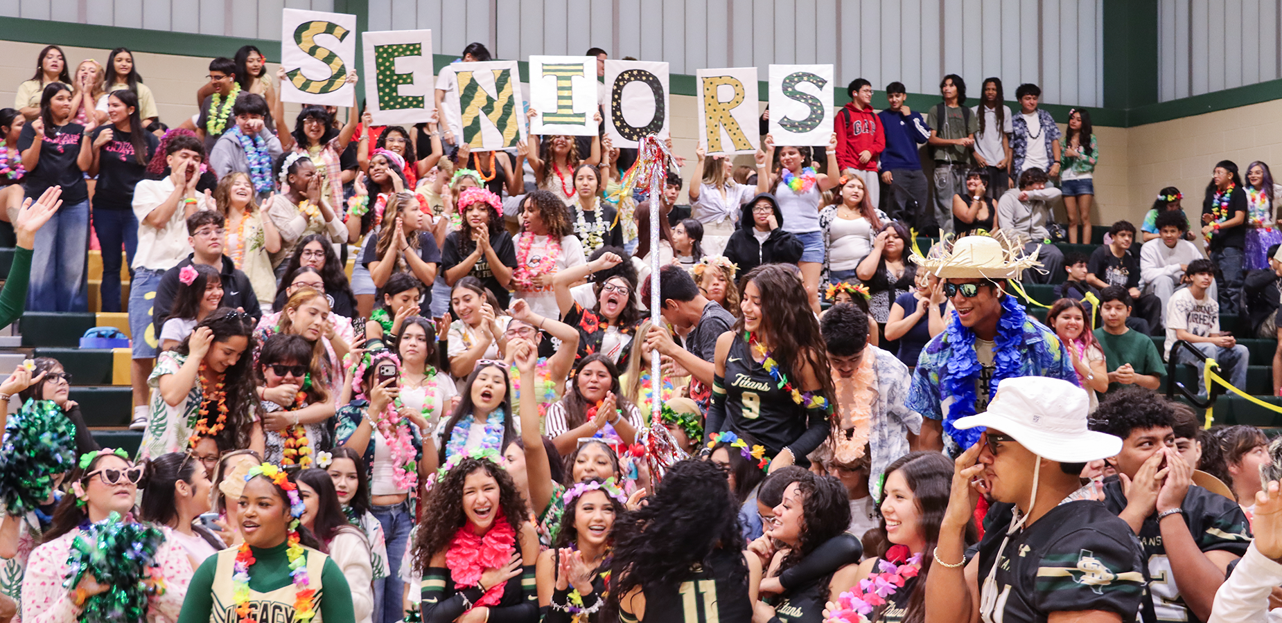 Energetic crowd of seniors celebrating with signs and colorful decorations in a gymnasium.
