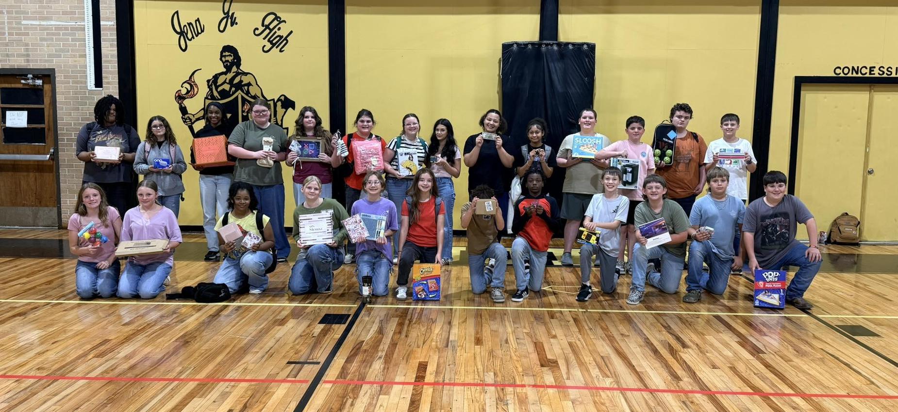 Group of students holding various items in a gymnasium setting.