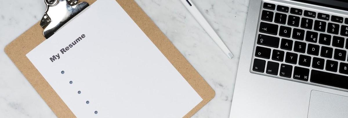 Clipboard with a resume on it next to a computer