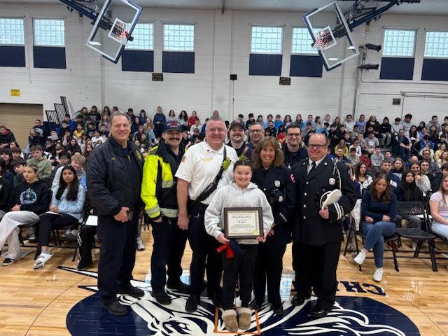 student holds an award with the fire department during school assembly