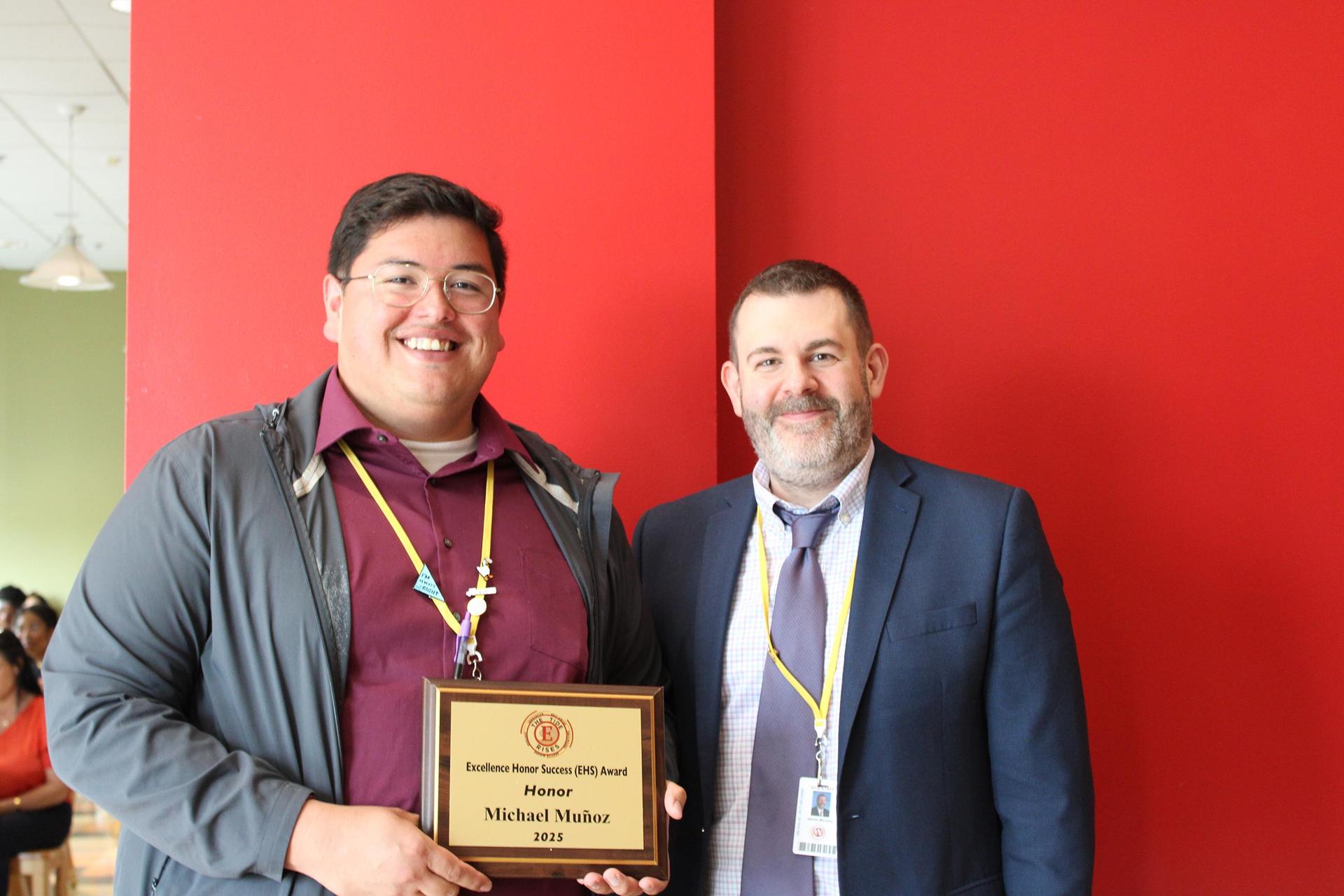 An educator holding an award certificate, standing next to a colleague