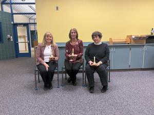 Three woman school board members seated holding bells they received