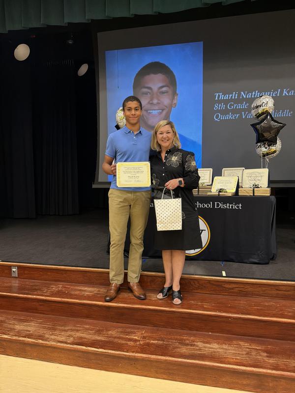 Student holding a certificate is standing next to his superintendent on a stage.