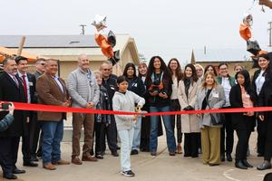 A student cuts the ribbon surrounded by staff, district leaders, and community members at the Green Schoolyards Project opening at John J. Doyle Elementary.