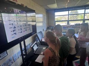 Deeply engaged third graders in a school classroom work to crack codes during a virtual satellite-repair simulation
