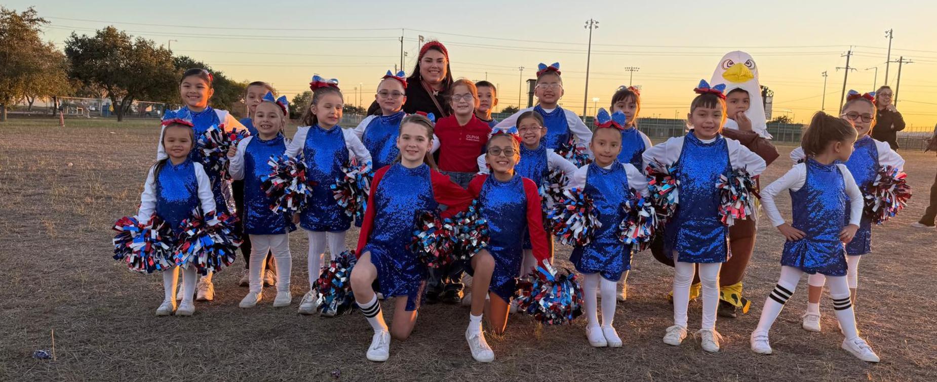 A cheerleading squad of young girls in blue outfits, holding pom-poms, posing on a field.