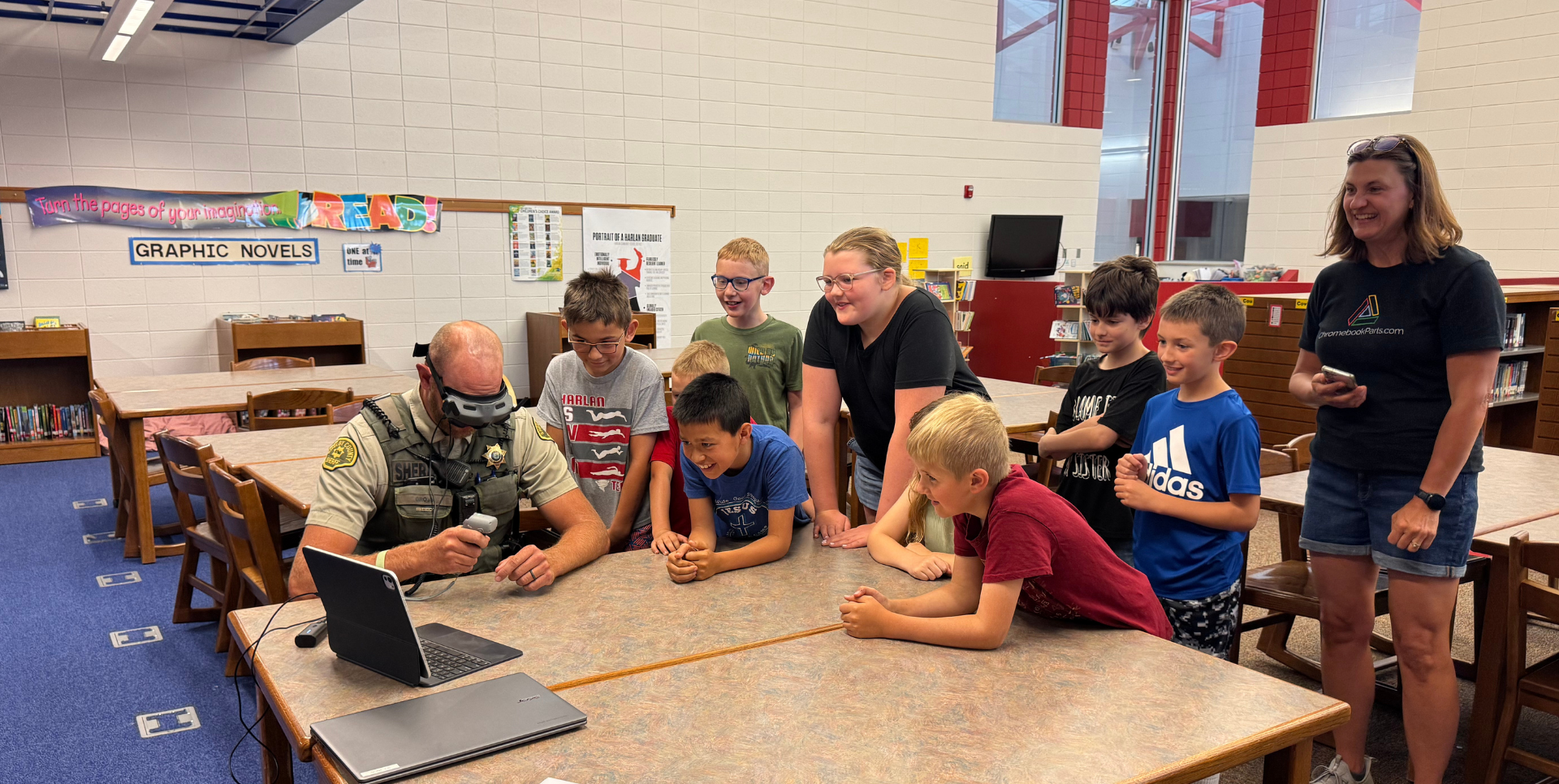 Children and a police officer engage with a laptop in a library.