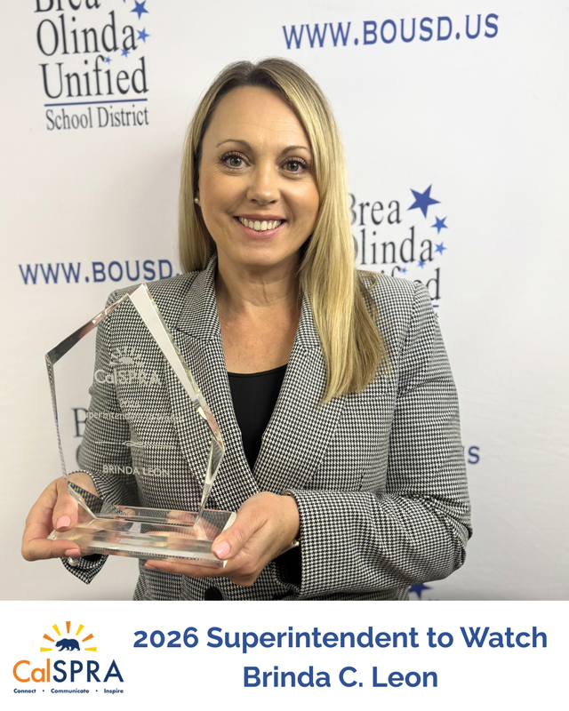 Brinda Leon stands in front of a BOUSD backdrop holding an award made of glass. Etched in the glass says 