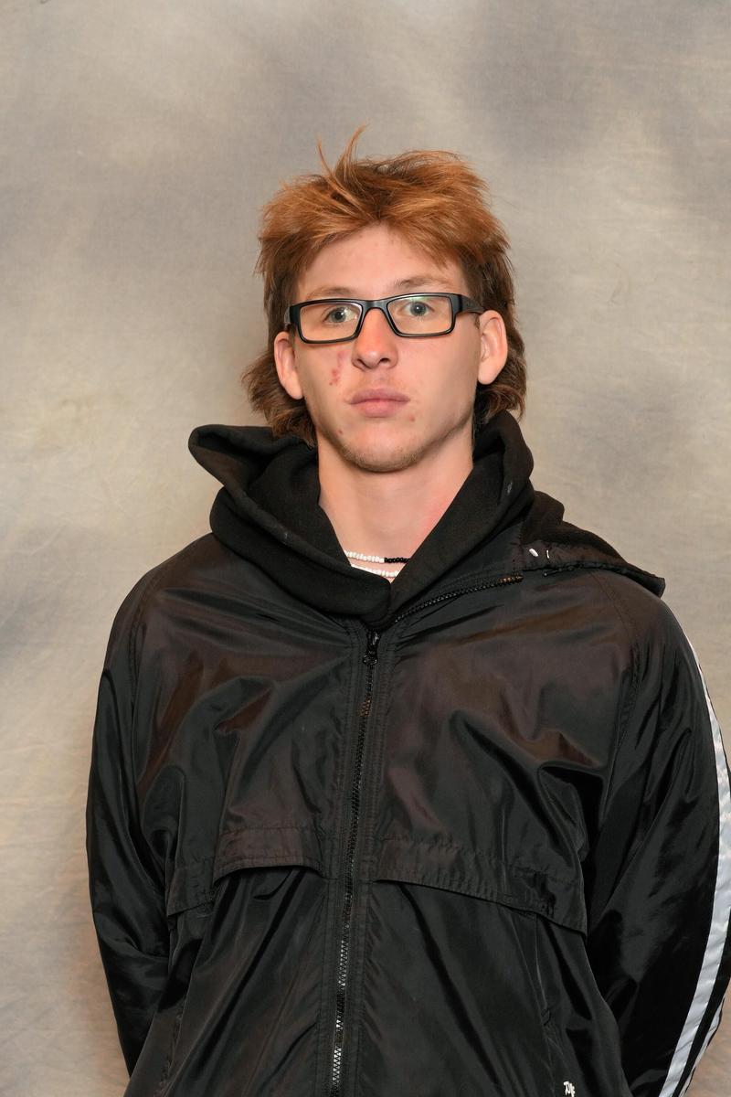 Male athlete with glasses stands with arms behind his back in front of a grey backdrop