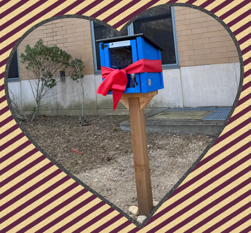 A blue Little Free Library wrapped with a red ribbon, set against a brick wall.