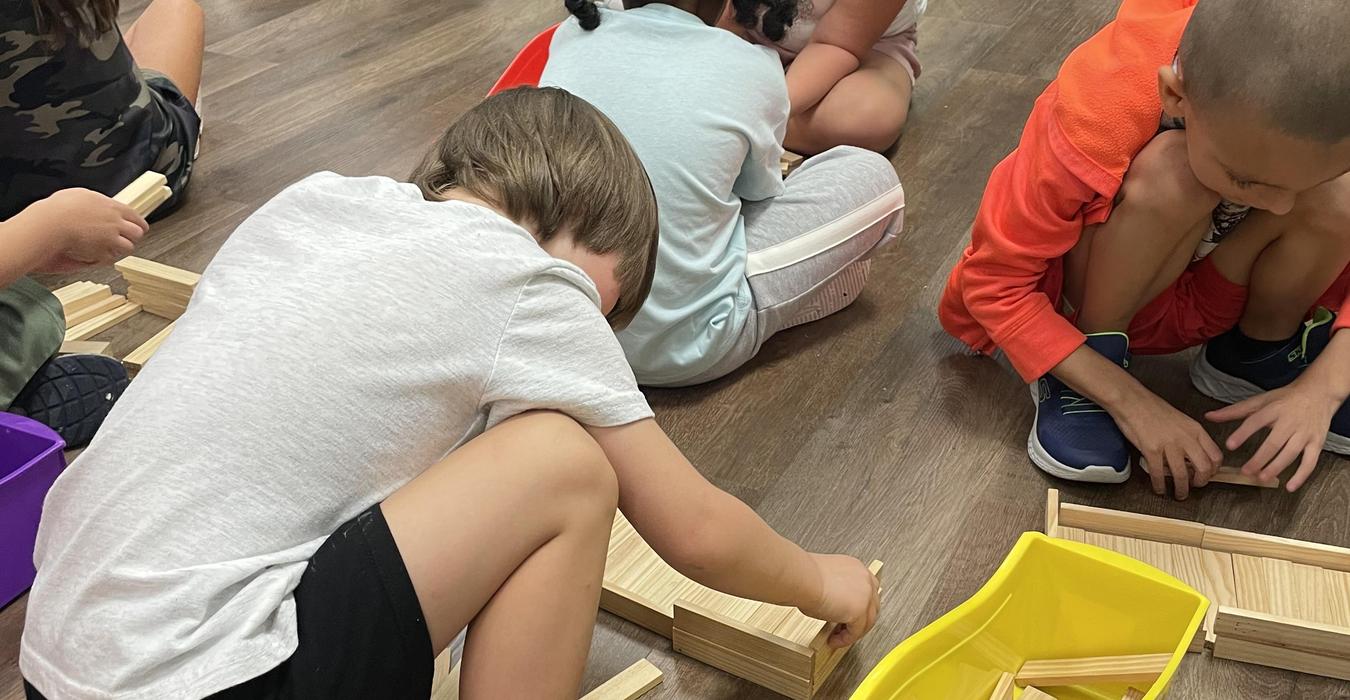 Children engaged in building with wooden blocks on a classroom floor.