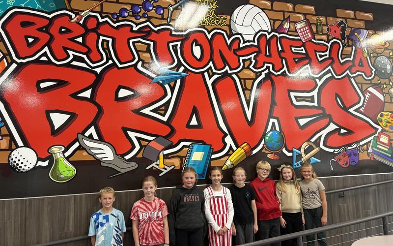 Group of children posing in front of a colorful mural that reads "BRAVES".