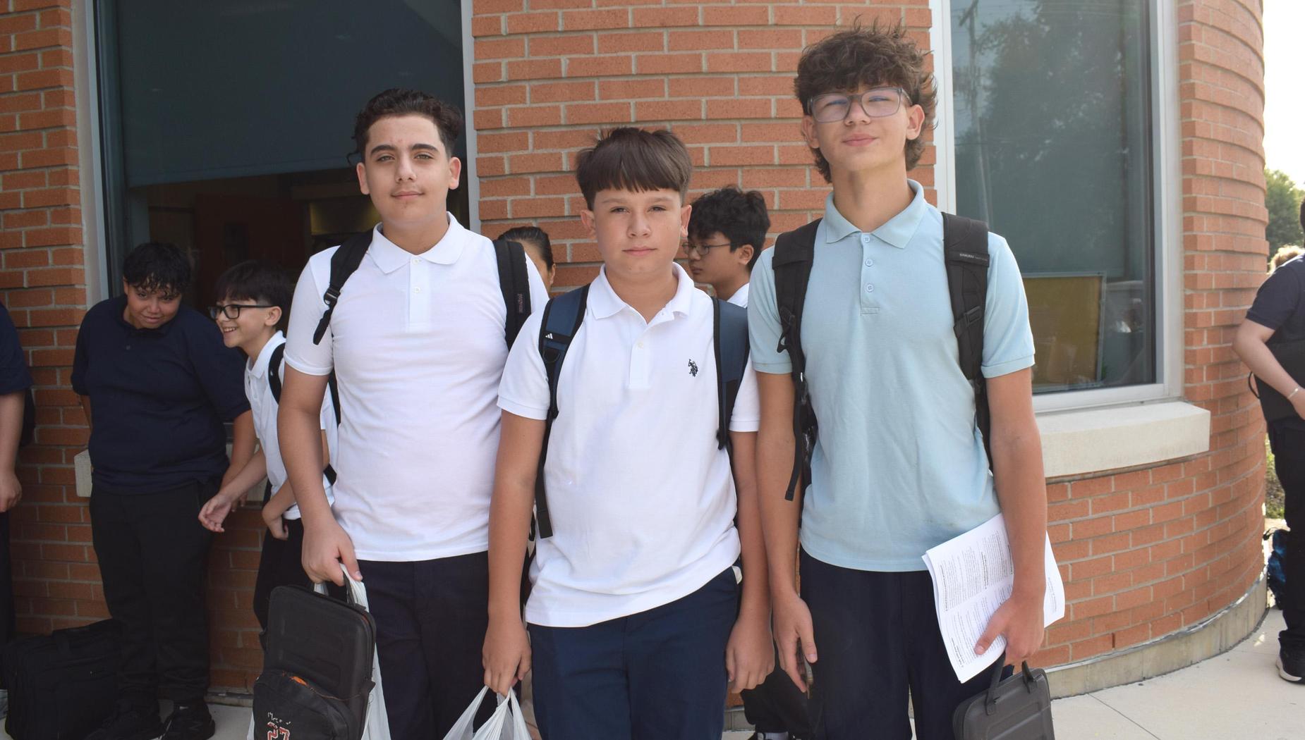 Three boys pose together in front of a school entrance, looking towards the camera.
