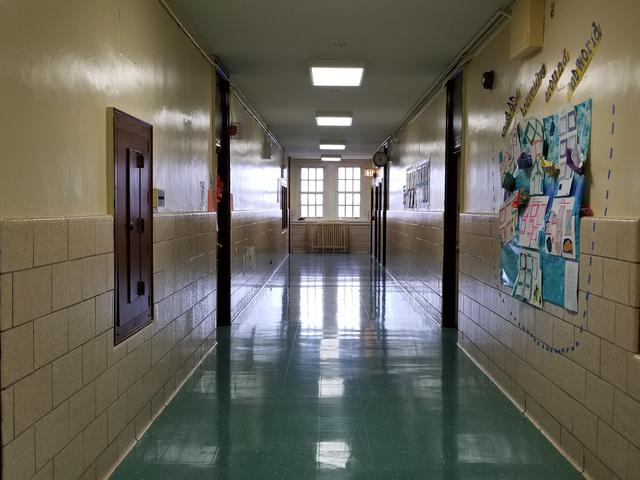 Long hallway with green floor, lockers, and bulletin board on the wall.