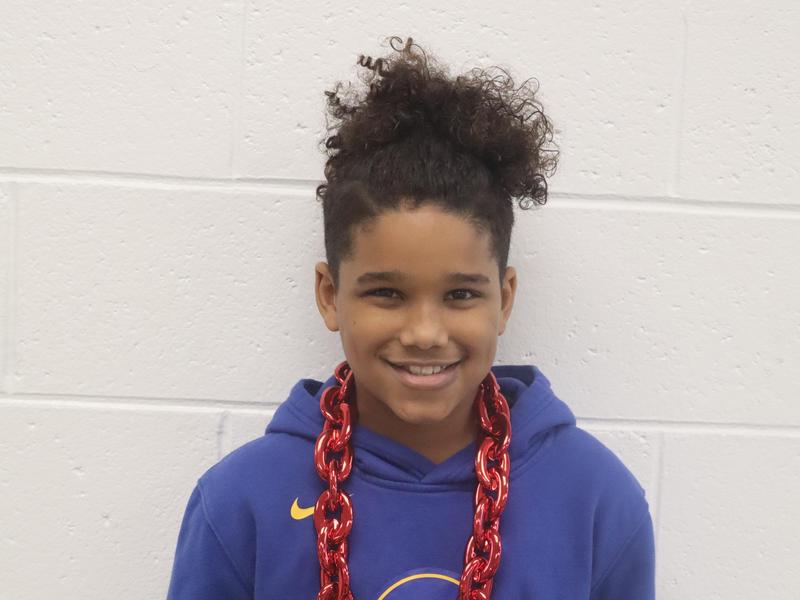 Smiling boy wearing a blue hoodie and large red chain necklace.