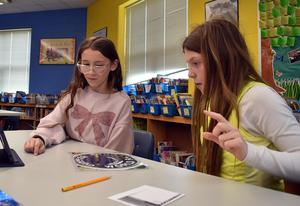 Two girls interacting with a tablet and discussing materials in a classroom.