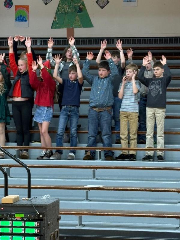 Children raise their hands while standing on bleachers in a choir performance.