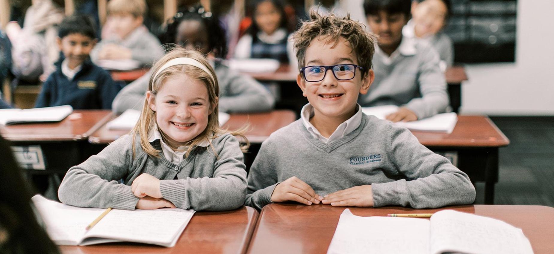 Two smiling elementary students sit together at their desks